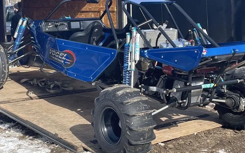 The blue Vogel Racing sand car with the Vogel Racing logo on the side panel, being loaded onto a trailer before the rebuild