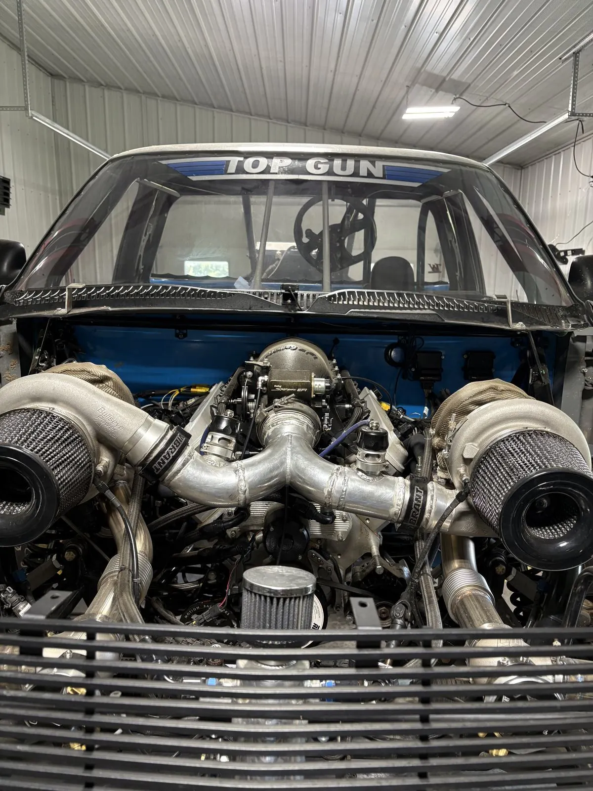 Head-on view of Top Gun's twin-turbo engine bay in the shop, TOP GUN banner on the windshield