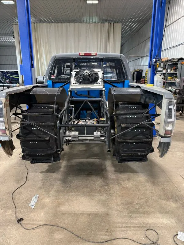 Top Gun on the lift in the shop, bed off showing the tube chassis and paddle tires