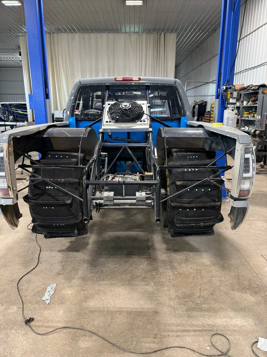 Top Gun on the lift in the shop from behind, bed off showing the tube chassis, paddle tires and blue cab
